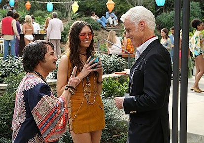 Two hippie style dressed people talking to a Roger at an outdoor party in Mad Men 