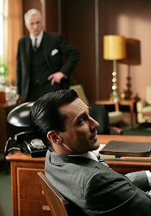 Don Draper sitting in his chair while Roger stands in the background in Mad Men 