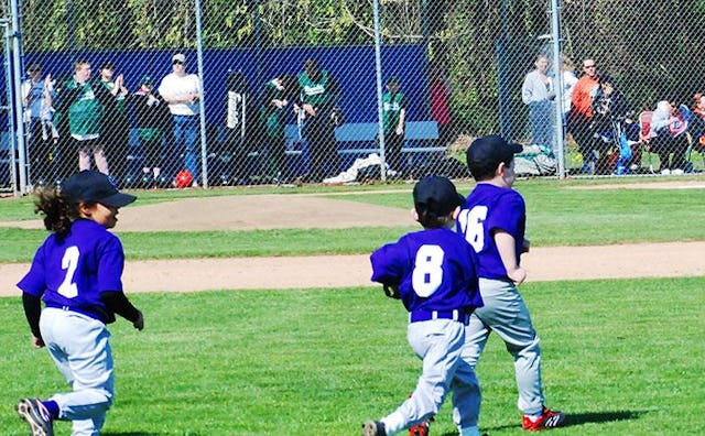 Three kids on a baseball field in blue shirts with the numbers 2, 8, and 16 on their backs, light bl...