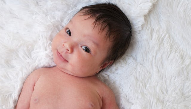 A newborn child lying on a white fur cover with a neutral facial expression
