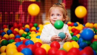 A little girl playing in the ball pit inside of an indoor playground