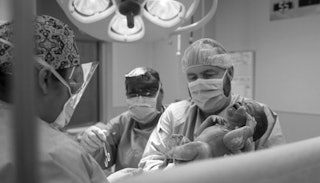A doctor holding a newborn after performing a C-section birth in black and white