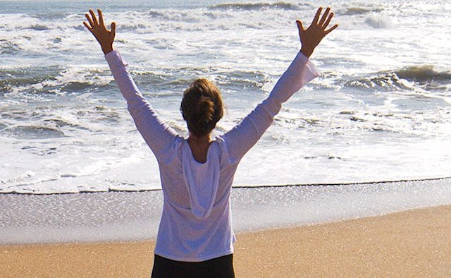 A woman who is 40 with her arms wide open looking at the sea
