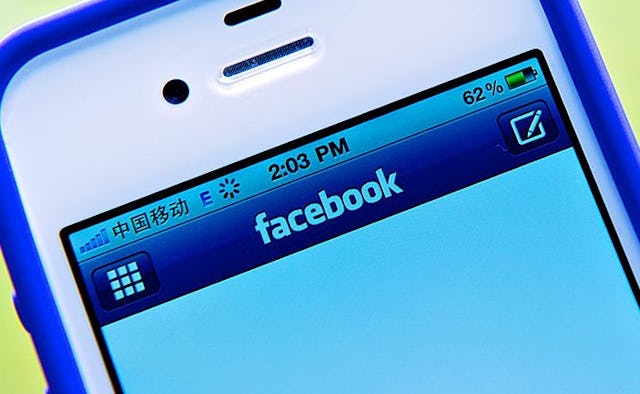 A zoomed-in upper display of a white-blue iPhone with the Facebook app opened on the screen