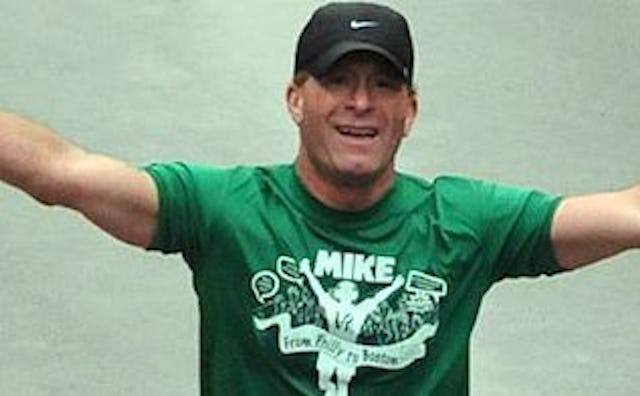 A man with his arms wide open in a green shirt while running the Boston Marathon