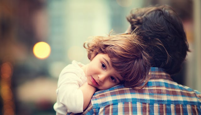 A father in a blue, burgundy, and yellow checked shirt holding his child in a white shirt