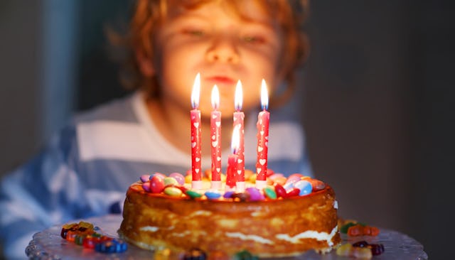 A small boy blowing candles of his fifth birthday cake