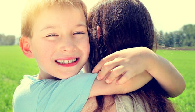 A smiling boy in a blue shirt who has autism hugging his mom