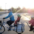 A man in a blue jacket and two toddlers riding on an extended 3-wheel bike 