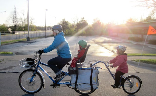 A man in a blue jacket and two toddlers riding on an extended 3-wheel bike