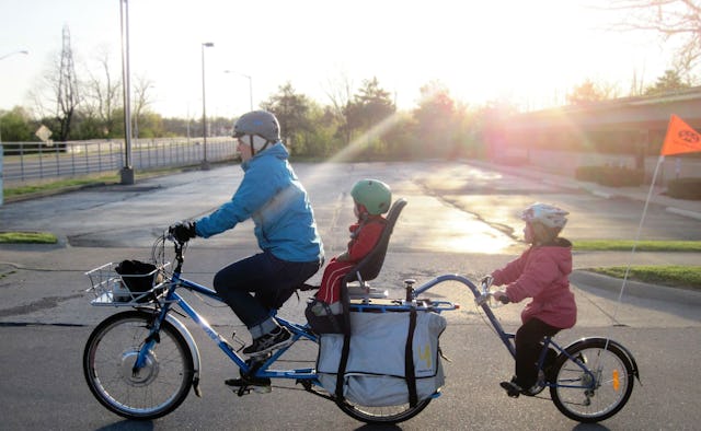 A man in a blue jacket and two toddlers riding on an extended 3-wheel bike 