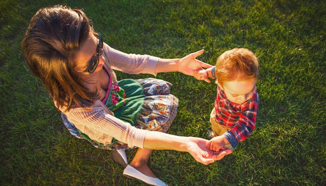A woman sitting down on the grass and playing with her baby boy