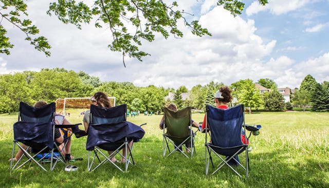 Four sports moms sitting in camo chairs and watching their sons playing football