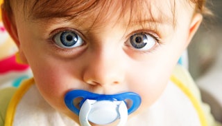 A close-up of a blue-eyed, brown-haired baby boy, sucking on a blue pacifier