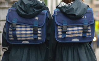 Two middle school girls in black hooded raincoats, both wearing navy blue backpacks 