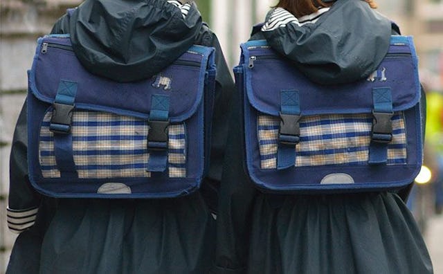 Two middle school girls in black hooded raincoats, both wearing navy blue backpacks