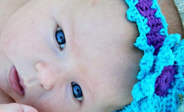 A close-up portrait of a baby with blue eyes and a blue knit headband