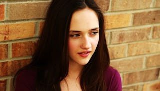 A brunette teen leaning against a brick wall 