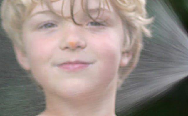 A blonde boy with water from a sprinkler over his face whose parents can't just send him out anymore