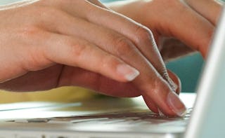 A close-up of a woman's hands typing on a white laptop's keyboard