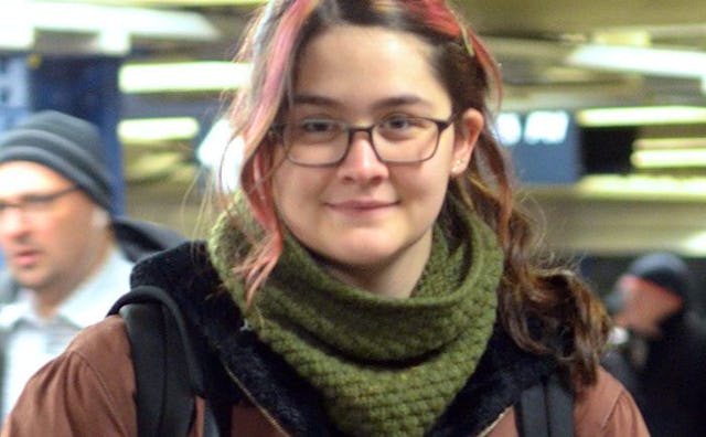 A Queer teen with pink highlights, wearing glasses, smiling for a photo