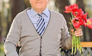 An older man dressed up for a date wearing a tie and holding a bouquet of flowers 