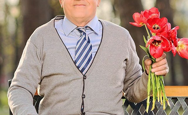 An older man dressed up for a date wearing a tie and holding a bouquet of flowers