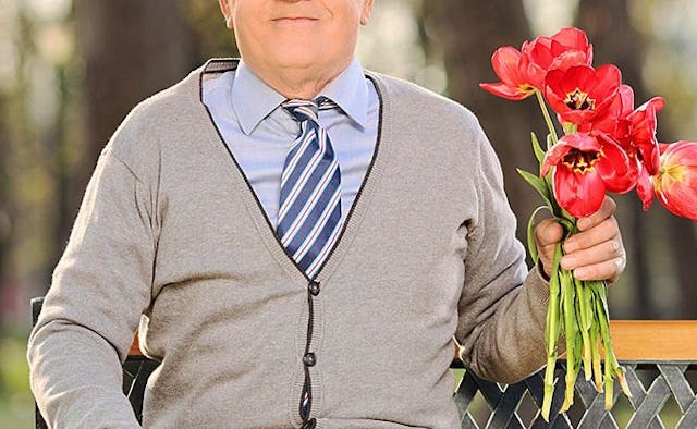 An older man dressed up for a date wearing a tie and holding a bouquet of flowers 