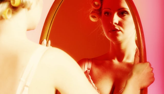 A blonde woman with curlers on her head is looking at herself in the mirror wondering who is the per...