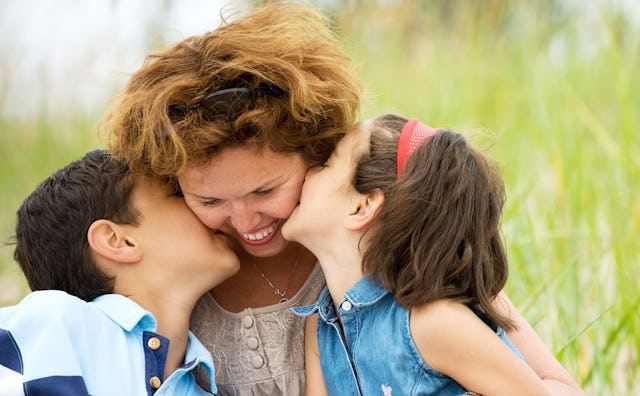 An old mom sitting while being kissed by her son and daughter