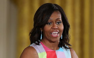 Michelle Obama speaking in front of a golden wall in a sleeveless color block top in blue, red and y...