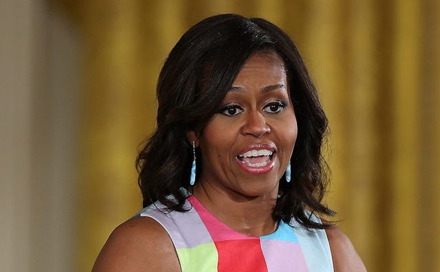 Michelle Obama speaking in front of a golden wall in a sleeveless color block top in blue, red and y...