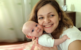 A millennial mom holding her newborn baby close to her face and smiling