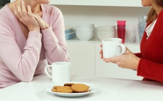 Two moms sitting at the kitchen table with two mugs and cookies on a plate