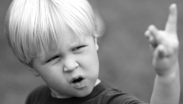 A blonde boy, holding his hand up and touching his thumb with his middle finger