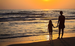 Woman and her boyfriend's daughter holding hands and enjoying a sunset on the beach 