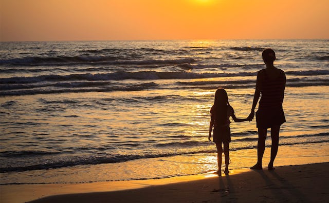 A woman and her boyfriend's daughter holding hands and enjoying a sunset on the beach