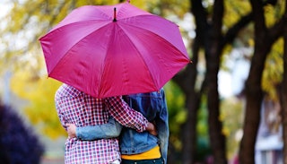 A husband and a wife under a purple umbrella, hugging and walking