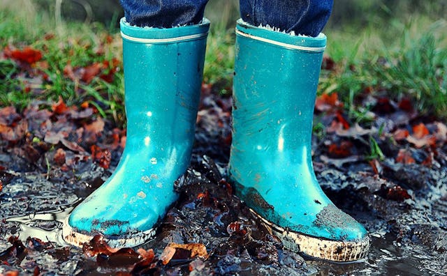 A tomboy teen standing in the mud in blue rain boots