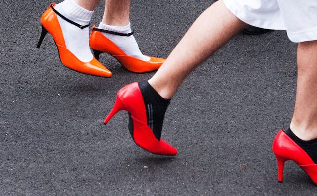 A woman in orange high heels and white socks and a woman in red high heels and black socks walking