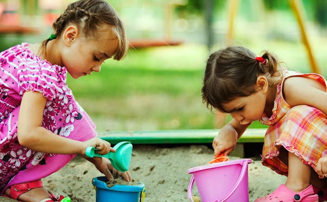 Two little girls playing in the sand with plastic buckets and shovels.