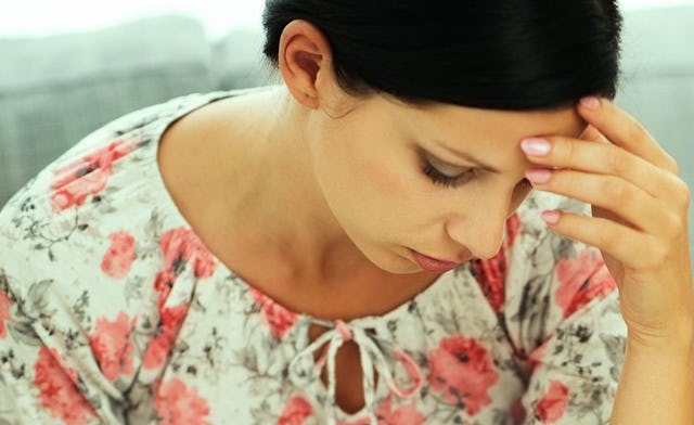 A brunette woman with anxiety in a floral top sitting and looking down
