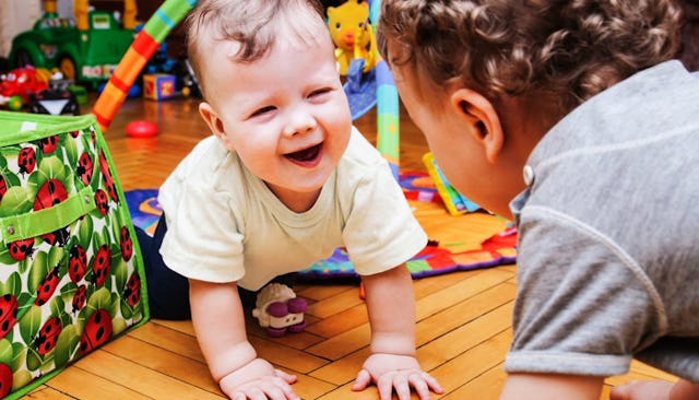 Two kids in a daycare smiling at each other while crawling