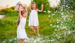 Two young sisters in white dresses playing outside with pillow feathers