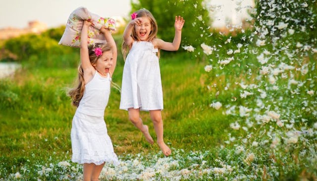 Two young sisters in white dresses playing outside with pillow feathers