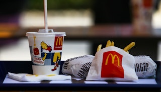 A McDonald's menu; a cup with a drink with a straw in it, a small bag with French fries, and two bur...