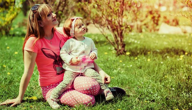 A mother with her daughter sitting on her knees in a garden, both of them looking up