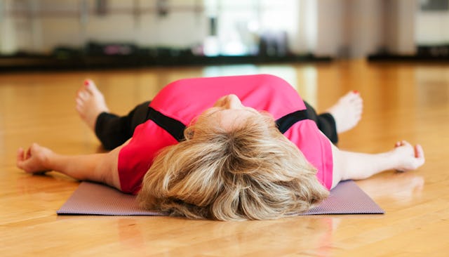 A blonde woman in a pink shirt and black yoga pants lying on a gray yoga mat after working out