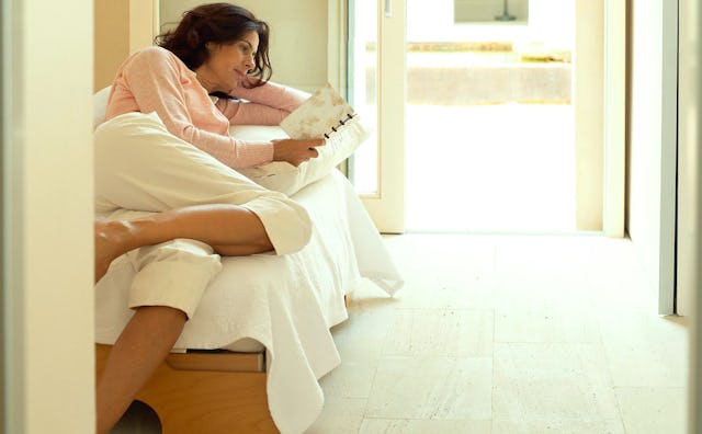 A woman lying on her bed sideways and reading a book