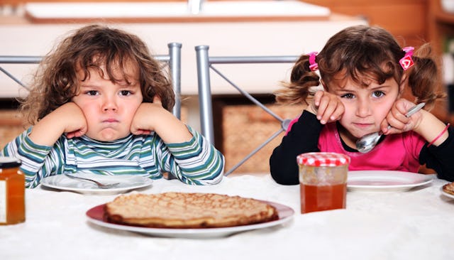 Two siblings sitting next to each other at breakfast while looking angry